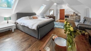 A modern loft bedroom with a large bed, skylight, and a kitchenette in the background. - This studio apartment is brilliant. (West Linton, near Edinburgh)