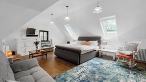 A bedroom with a bed, a gray sofa, a rocking chair, a desk with a computer, and a window with a view. - This studio apartment is brilliant. (West Linton, near Edinburgh)