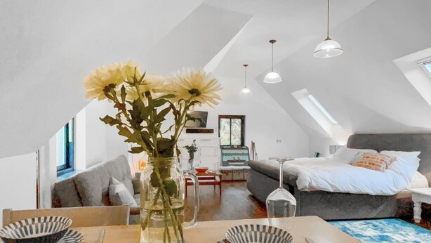 A dining area with a table set for two, a vase with flowers, and a view of a bedroom with a bed and a window. - This studio apartment is brilliant. (West Linton, near Edinburgh)