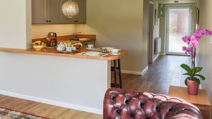 A modern kitchen with a central island, a dining area with a leather ottoman, and a hallway leading to a door. - 1 bedroom accommodation in Strumpshaw, near Norwich (Strumpshaw, near Norwich)