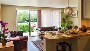 A modern kitchen with a dining area, featuring a leather sofa, a bar stool, and a view of the garden. - 1 bedroom accommodation in Strumpshaw, near Norwich (Strumpshaw, near Norwich)