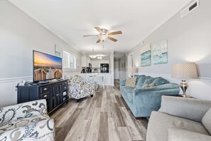 A living room with a sofa, a patterned armchair, a coffee table, a TV, and a ceiling fan.