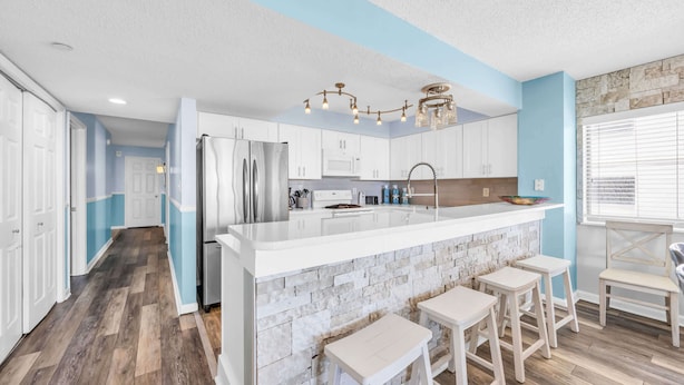 A modern kitchen with white cabinets, a central island, and bar stools.