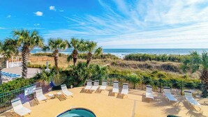 A beachside hotel with a pool, sun loungers, and palm trees.