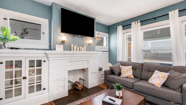 A living room with a fireplace, a sofa, a coffee table, and a TV mounted on the wall. - 3 Bed 2 Bath by College Hill w/ Fitness Room (Wichita)