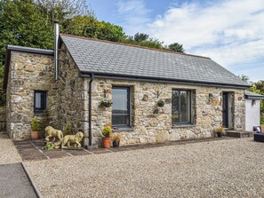 A stone house with a gravel driveway, two windows with shutters, and a small garden area with potted plants and a statue. - 1 bedroom accommodation in Lanner, near Falmouth (Lanner, near Falmouth)