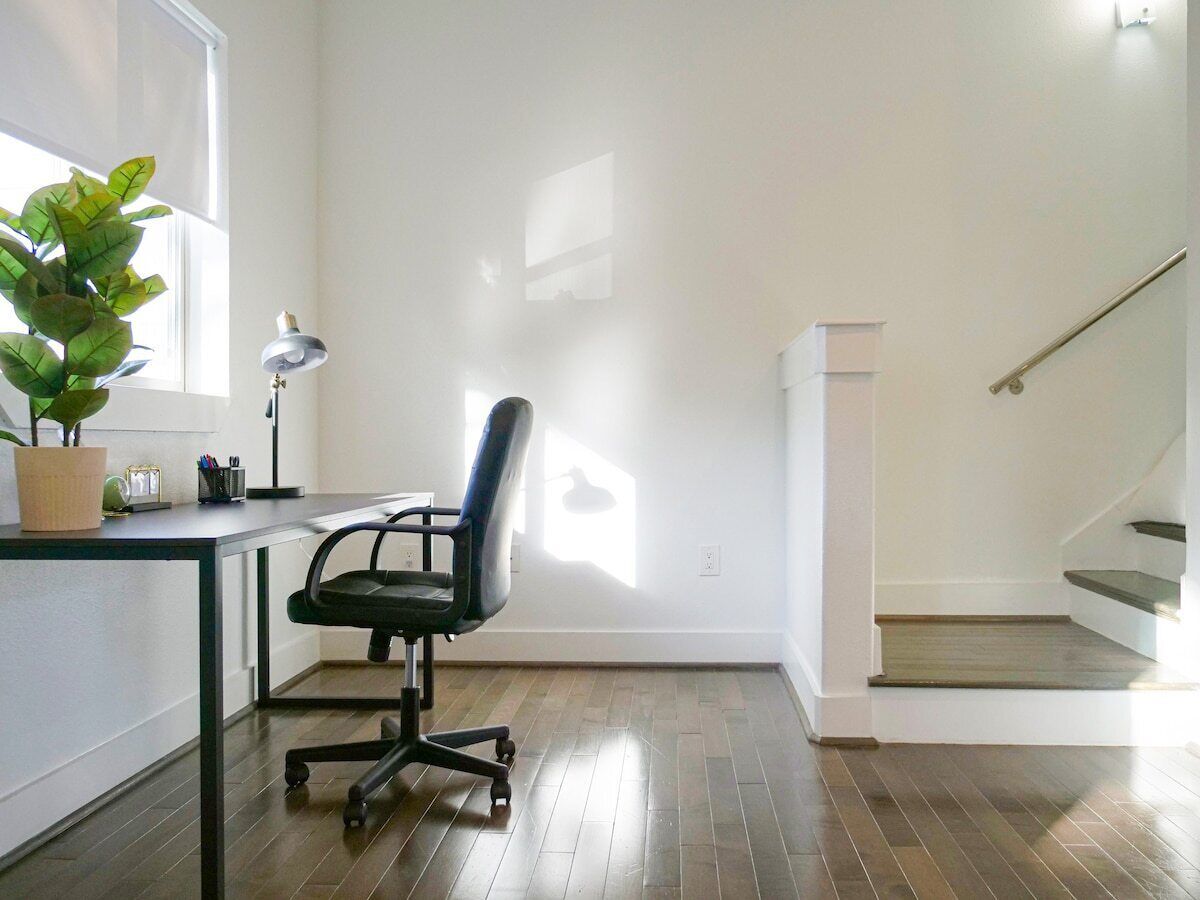 A room with a desk, chair, potted plant, and a staircase.