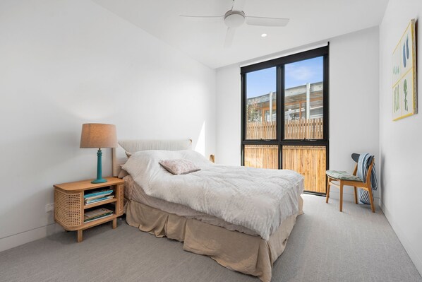 A bedroom with a large window, a bed, a nightstand, and a chair. - Gorgeous George Barwon Heads (Barwon Heads)