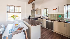 Une cuisine moderne dotée d’un îlot central, de poutres en bois et d’un coin repas avec une table et des chaises.
