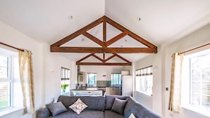 Un salon moderne avec un grand canapé d’angle, des poutres en bois au plafond et une vue sur la cuisine.