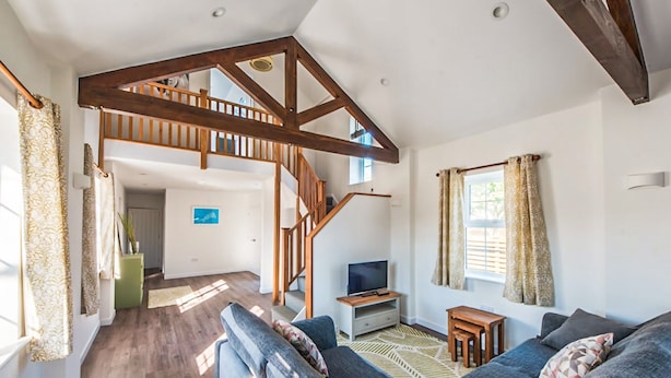 Un vaste espace de vie comprenant un escalier en bois, un ensemble de canapés, un téléviseur et une fenêtre avec des rideaux.