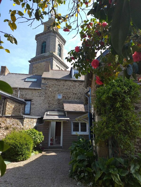 A stone building with a tower, a gravel driveway, and a small garden with roses.