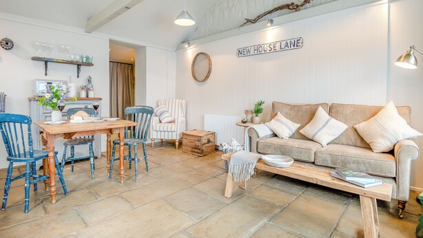 A cozy living room with a wooden table, striped armchair, and a beige sofa with pillows. A sign on the wall reads "NEW HOUSE LANE." - 2 bedroom accommodation in Walsingham, Wells-next-the-Sea (Walsingham, Wells-next-the-Sea)