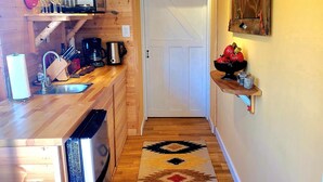 Una cocina compacta con muebles de madera, un horno integrado y una cafetera. Una alfombra estampada cubre el suelo, guiando hacia una puerta.