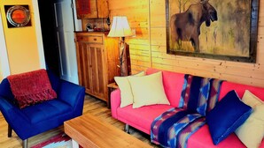 Una habitación acogedora con un sillón azul, un sofá rosa y una mesa de comedor de madera.