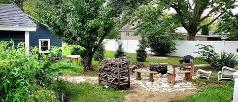 A backyard with a stone patio, wooden furniture, and a variety of plants.