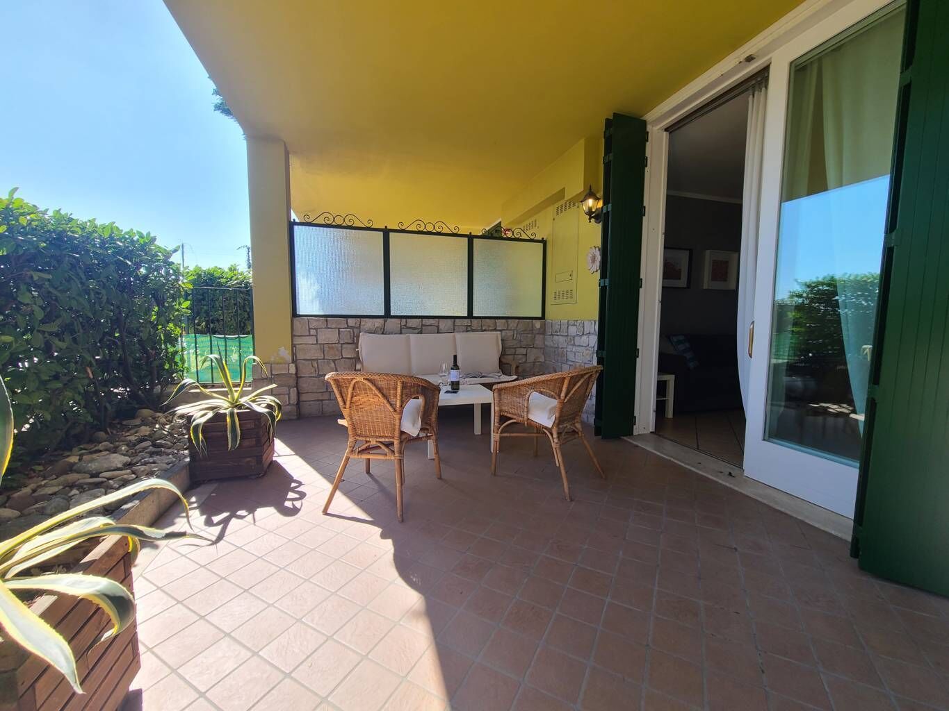 A patio area with a table and chairs, a stone wall, and a sliding glass door leading to an interior space.