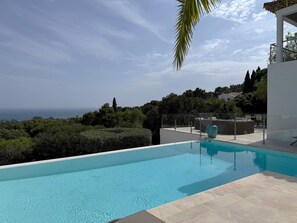 Una piscina amb vistes al mar, envoltada de vegetació i un edifici modern.