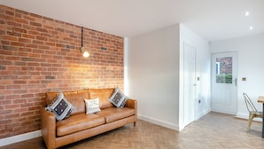 A room with a brick wall, a leather sofa with patterned cushions, a wooden herringbone floor, and a white door. - 5 bedroom accommodation in Ashbourne (Ashbourne)