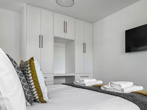 Un dormitorio con cama, armario blanco y televisor de pantalla plana en la pared.