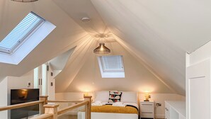 A bedroom with a sloped ceiling, skylights, a bed with a yellow blanket, bedside lamps, a TV, and a wardrobe. - 5 bedroom accommodation in Ashbourne (Ashbourne)