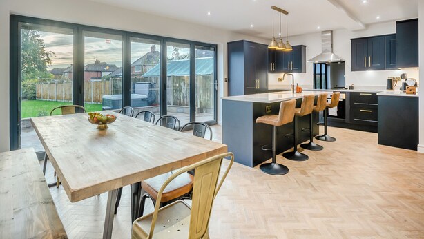 A modern kitchen with a large island, dark cabinetry, and a dining area with a wooden table and chairs. - 5 bedroom accommodation in Ashbourne (Ashbourne)