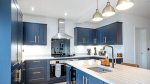 A modern kitchen with dark blue cabinets, a large island with a sink, and stainless steel appliances. - 5 bedroom accommodation in Ashbourne (Ashbourne)