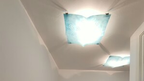 Una habitación con una silla blanca, una lámpara en el techo y suelo de baldosas.