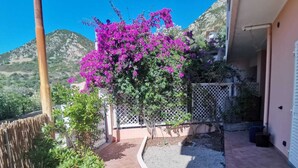 Un balcón con vistas a un paisaje montañoso, un jardín con buganvillas y una cerca blanca.