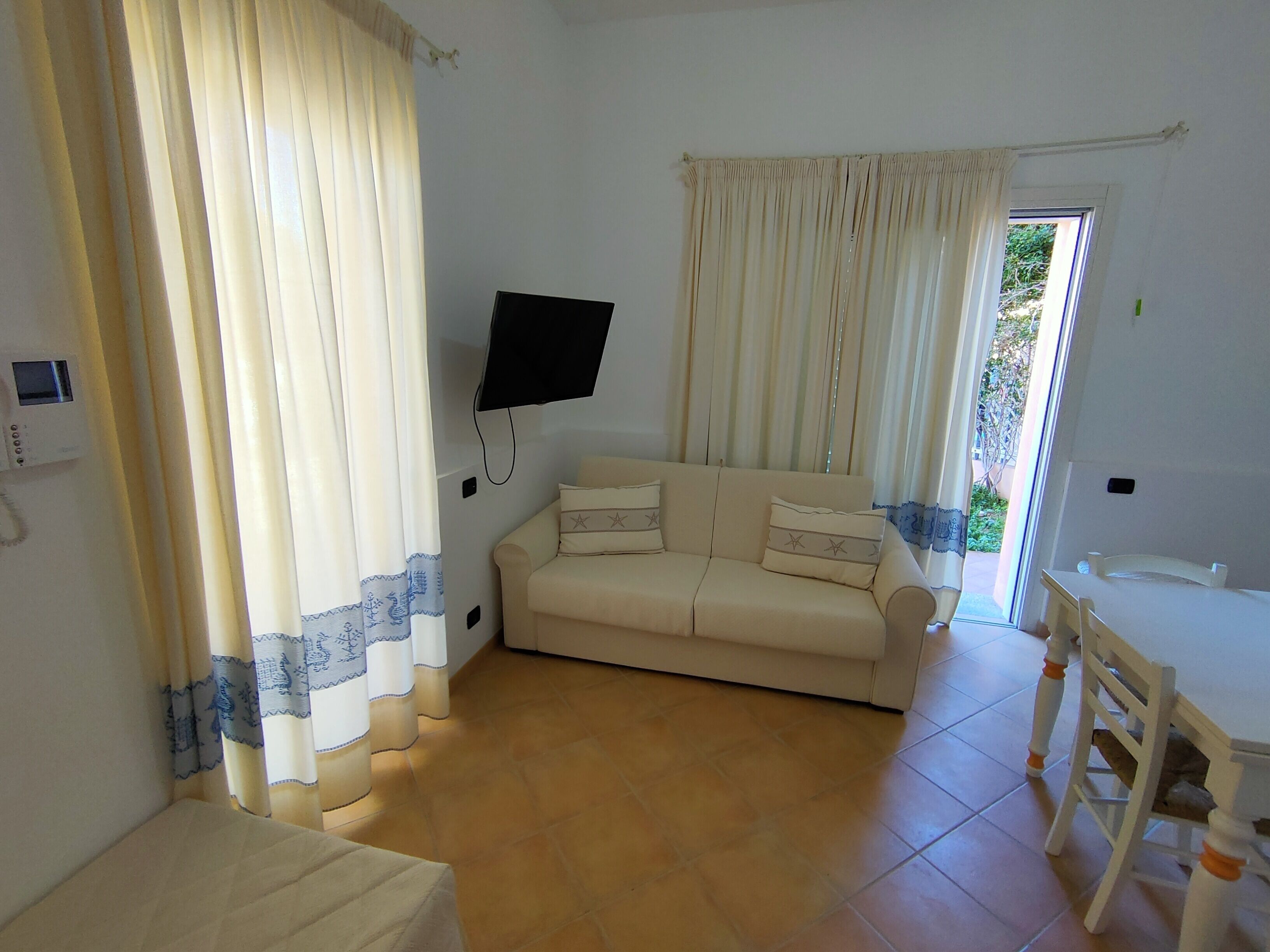 Un salon avec un canapé beige, un téléviseur fixé au mur et une table à manger avec des chaises.