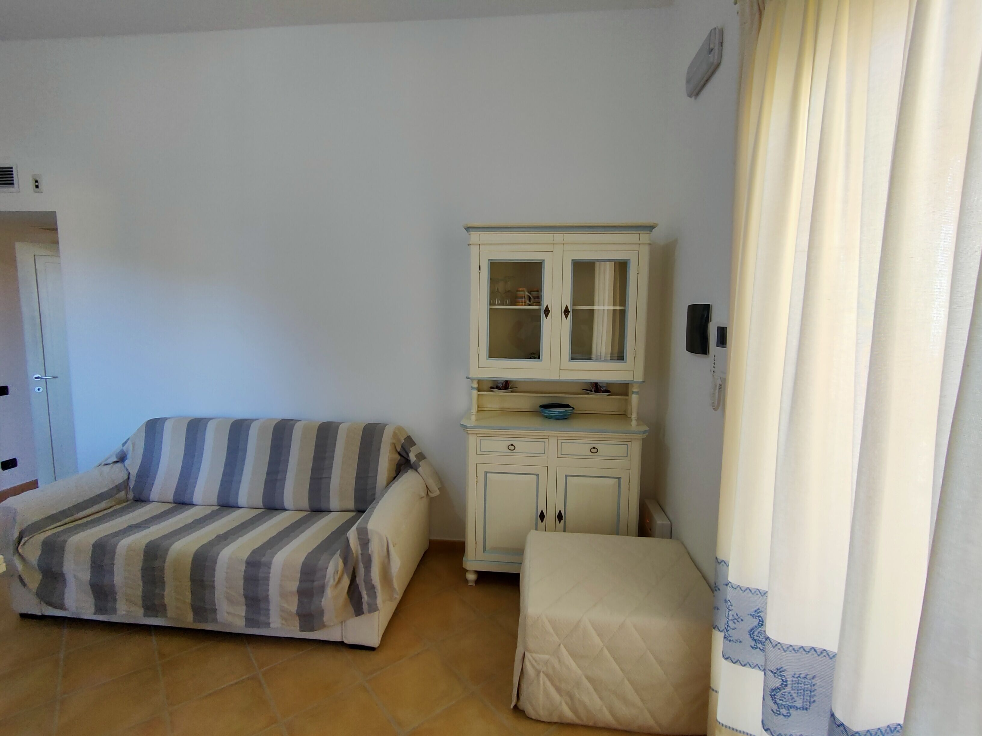 A room with a striped sofa, a cabinet with glass doors, and a curtain.