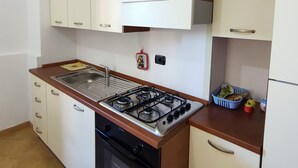 Una cocina con gabinetes blancos, estufa a gas, un fregadero y un refrigerador pequeño.