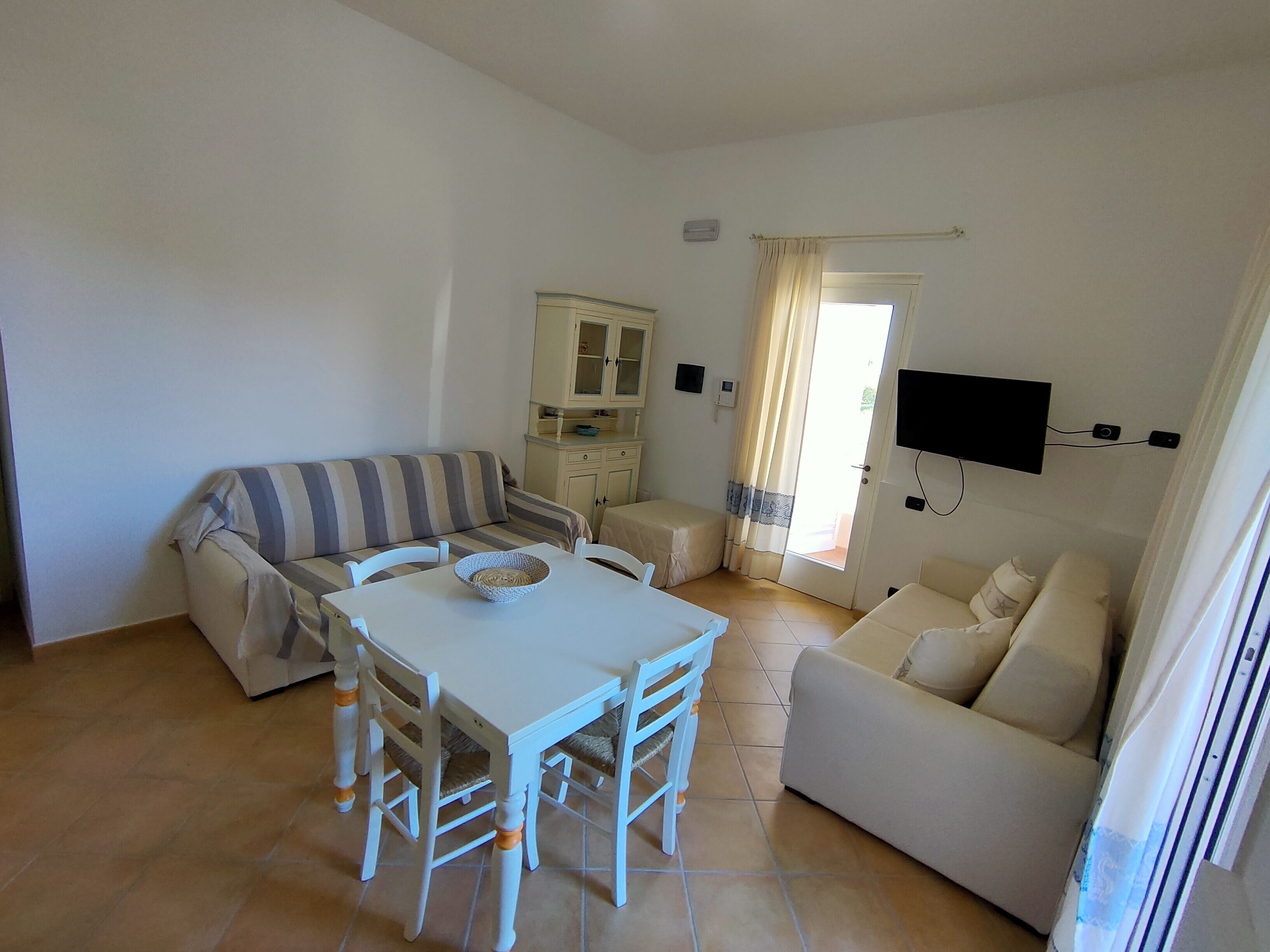 Un espace de vie compact comprenant un canapé à rayures, une table à manger avec des chaises, un petit coin cuisine et un téléviseur fixé au mur.