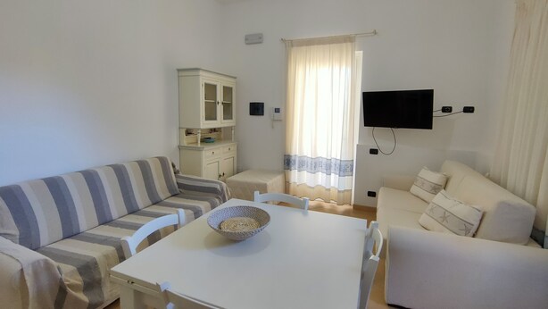 Una sala de estar con un sofá a rayas, un sillón blanco, una mesita con un cuenco, un aparador y un televisor montado en la pared.