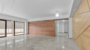 Amplia habitación de hotel moderna con suelo de mármol pulido, pared decorada con ladrillo y grandes puertas correderas de vidrio que dan a un balcón.