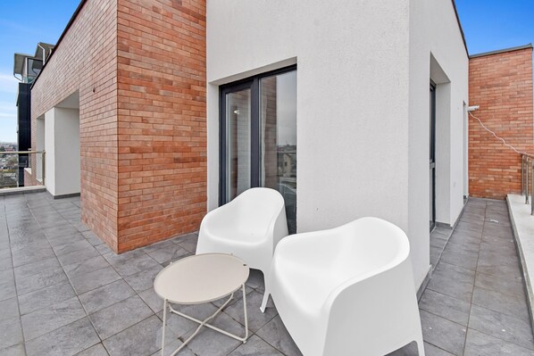 A modern building with a brick facade, a glass door, and a small outdoor seating area with two white chairs and a table.