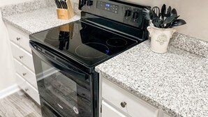 A kitchen with a black stove, white cabinets, and granite countertops.