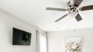 A bedroom with a bed, a ceiling fan, a flat-screen TV, and a painting on the wall.