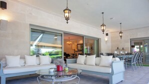 A modern outdoor living area with a white sofa set, a glass coffee table, and hanging lanterns.