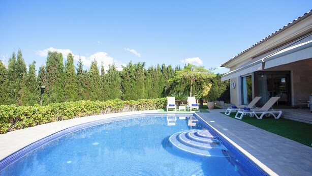 A swimming pool with a tiled edge, surrounded by a lawn and trees.