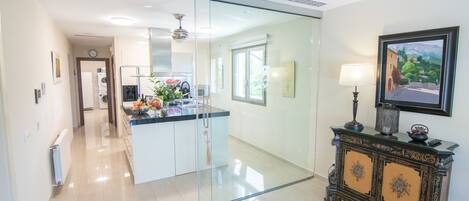 A modern kitchen with a glass partition, a central island, and a decorative cabinet with a lamp.