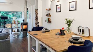 Een moderne woonkamer met een houten eettafel, een open haard, een televisie en uitzicht op groen.