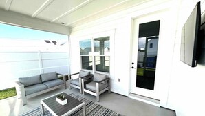 A covered patio with a gray sofa, a coffee table, and a striped rug.