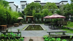 A courtyard with a central pond, surrounded by tables and chairs, and a building in the background.