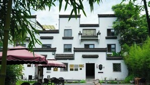 A traditional building with multiple windows and balconies, a courtyard with a small pond, and outdoor seating with umbrellas.