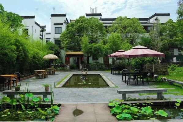 A courtyard with a central pond, outdoor seating, and a building in the background.