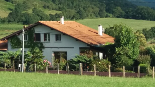Una casa blanca con techo rojo, rodeada de vegetación exuberante y montañas al fondo.
