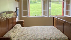 Un dormitorio con una cama, una ventana con contraventanas abiertas, un radiador y un marco de cuadro en la pared.