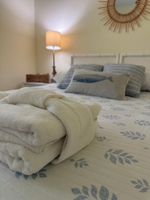 A neatly made bed with a folded white towel, a bedside table with a lamp, and a wall-mounted mirror. - New rental overlooking Plantation Course 9th tee box. 1500 sq feet, smoke free. (Edisto Island)