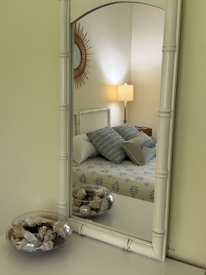 Une chambre à coucher avec un lit, des oreillers, une lampe, un élément décoratif mural et un bol rempli de coquillages.